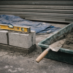 稲沢市の丸岩天祥店舗玄関前。コンクリートブロックと左官道具が並ぶ施工中の様子。